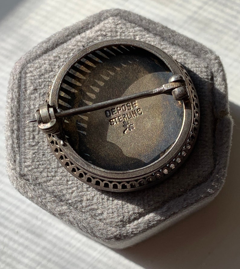 K&ouml;nnte beinhalten: Eine silberne Brosche mit einem runden, filigranen Design. Die R&uuml;ckseite der Brosche tr&auml;gt die Worte "Depose Sterling" und einen Stern.