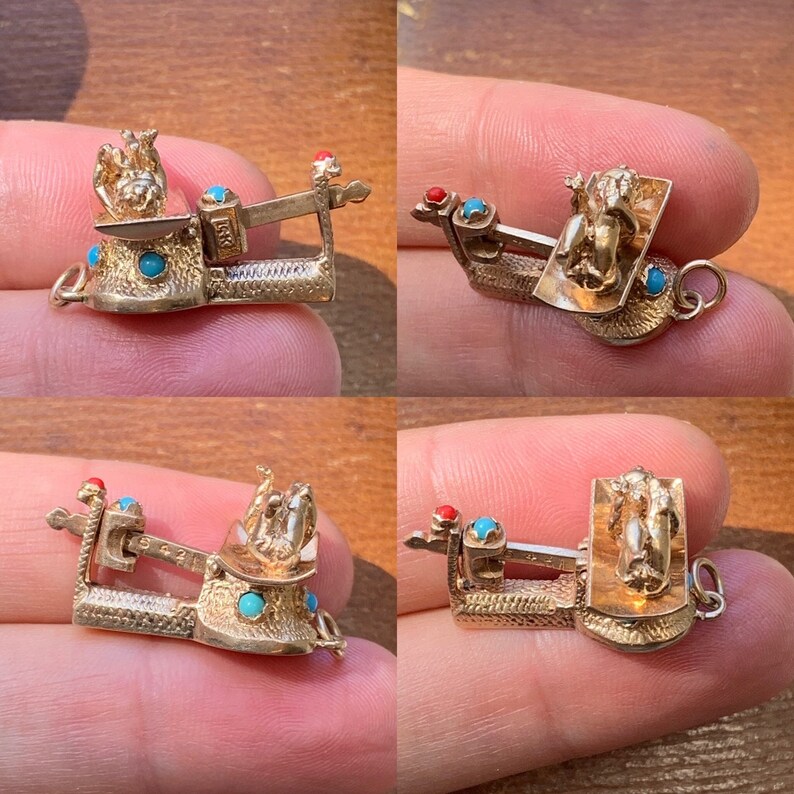 Op de afbeelding: Een goudkleurige bedel in de vorm van een weegschaal, met turquoise en rode accenten. De weegschaal heeft ingewikkelde details en een klein figuur bovenop. De bedel wordt in een hand gehouden.