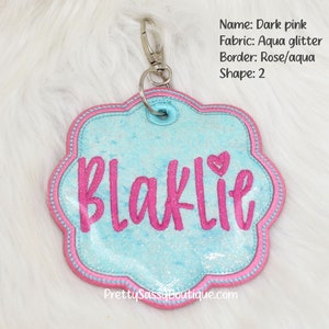 May include: Pink and aqua glitter personalized name tag with the name "Blaklie" in pink lettering. The tag is shaped like a flower and has a pink border.