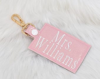 May include: A pink glitter keychain with a gold clasp and a white embroidered label that reads "Mrs. Williams".