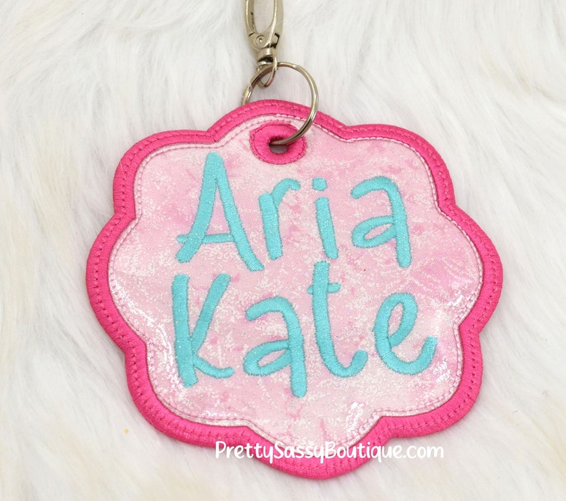 K&ouml;nnte beinhalten: Personalisiertes Namensschild in Pink und T&uuml;rkis mit den Namen "Aria Kate" auf einem pinkfarbenen, glitzernden Hintergrund. Das Schild ist an einem silbernen Schl&uuml;sselring befestigt.