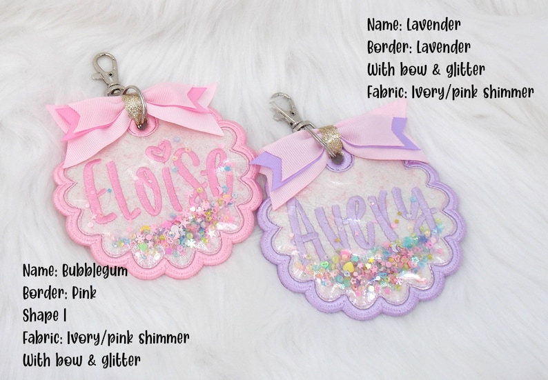 K&ouml;nnte beinhalten: Zwei personalisierte Schl&uuml;sselanh&auml;nger mit Glitzer und Schleifen. Der Schl&uuml;sselanh&auml;nger links ist rosa mit dem Namen "Eloise" und der Schl&uuml;sselanh&auml;nger rechts ist lila mit dem Namen "Avery".