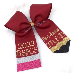 May include: Burgundy bow with gold glitter lettering. One side says "2022 BSFCS" and the other side says "Next chapter M.E.D."