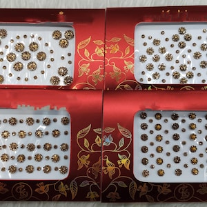 Könnte beinhalten: Vier rote Boxen mit goldenen Blumendesigns, jede mit einer Folie kleiner goldener und transparenter Kleberhinestones.