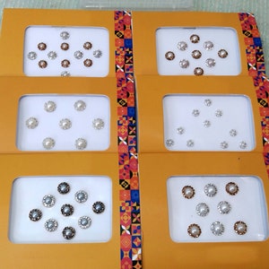 Könnte beinhalten: Sechs Blätter weißen Papiers mit einem bunten Muster an der Kante. Jedes Blatt hat ein anderes Design aus weißen, perlmuttartigen Aufklebern, die symmetrisch angeordnet sind.