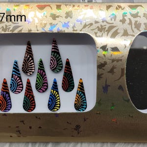 Puede incluir: Un paquete de pegatinas decorativas para uñas. Las pegatinas tienen forma de lágrima con diseños coloridos y estampados. El paquete es dorado con el texto "No.1-17mm".