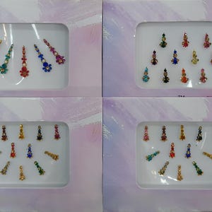 May include: Four rectangular white display cards featuring assorted decorative bindi stickers. Each card contains multiple adhesive bindis in various shapes, sizes, and colors, including gold, red, blue, green, and pink, accented with small rhinestones.