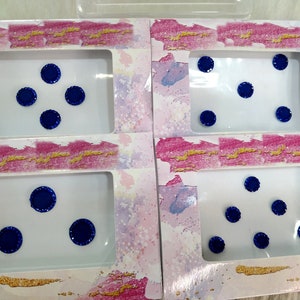 May include: Four clear plastic containers with white lids, each containing blue jeweled stickers. The stickers are arranged in different patterns.