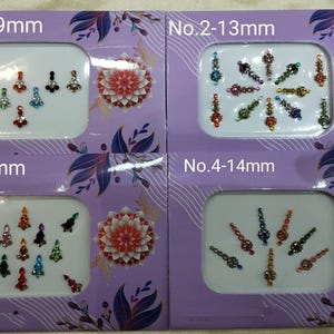 Puede incluir: Cuatro paquetes de pegatinas corporales adhesivas, coloridas y adornadas con joyas. Cada paquete tiene un tamaño y estilo de pegatina diferente. Los paquetes están etiquetados con los números 1-4 y el tamaño de las pegatinas en milímetros. No. 1-9 mm, No. 2-13 mm, No. 3-9 mm, No. 4-14 mm.