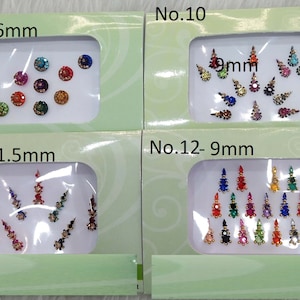 Puede incluir: Cuatro paquetes de pegatinas bindi con joyas de colores. Los paquetes están etiquetados con números y tamaños en milímetros. No. 9 - 6mm, No. 10 - 9mm, No. 11 - 1,5mm, No. 12 - 9mm.