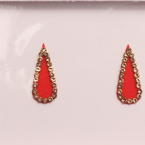 Puede incluir: Cuatro pegatinas bindi de color rojo en forma de lágrima con ribete de purpurina dorada. Las pegatinas miden 18 mm.