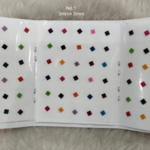 Puede incluir: Un conjunto de 36 pequeñas piedras de imitación de forma cuadrada, autoadhesivas, en varios colores, incluyendo negro, blanco, rojo, azul, verde, amarillo y morado. Las piedras de imitación están dispuestas en un patrón de cuadrícula sobre un fondo blanco. El texto "No. 1 3mm x 3mm" está impreso en la parte superior de la página.