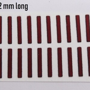 Può includere: Un foglio rettangolare bianco con 24 forme rettangolari bordeaux, ciascuna lunga 1,2 cm, disposte a griglia. Le forme bordeaux hanno un aspetto leggermente strutturato. Il testo "12 mm long" è in alto a sinistra.