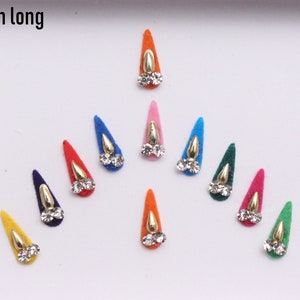 Puede incluir: Un conjunto de 12 pegatinas bindi de colores vivos, con forma de lágrima, con respaldo de fieltro y detalles de strass dorados y transparentes. 7 mm de largo.