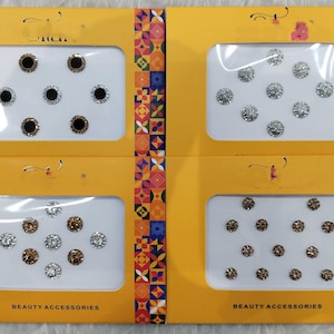 Könnte beinhalten: Vier Sets von Schönheitsaccessoires, jeweils in einer gelben Verpackung. Jedes Set enthält mehrere kleine, runde, dekorative Artikel in verschiedenen Farben, darunter Schwarz, Silber und Gold. Der Text "BEAUTY ACCESSORIES" ist sichtbar.