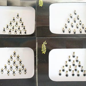 May include: Four black and white cards with a triangle design of black and white rhinestones. Each card has a gold leaf design in the corner.
