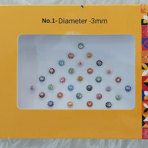 May include: A collection of small, colorful, flower-shaped decorative items, each approximately 0.12 inches in diameter, presented in a yellow box. The box has a rectangular window displaying the items, with the text "No.1- Diameter -3mm".