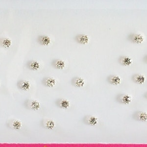 May include: A white plastic container with rows of small, clear rhinestones. The rhinestones are arranged in a grid pattern.