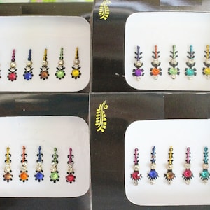 Può includere: Quattro set di sei adesivi bindi con gioielli colorati, ogni set disposto in una fila su uno sfondo bianco.