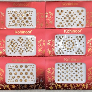 Könnte beinhalten: Vier rot-weiß gemusterte Karten mit dem aufgedruckten Wort "Kohinoor". Jede Karte enthält ein weißes Rechteck mit einer Vielzahl kleiner, runder, selbstklebender Steine in Gold und Klar.