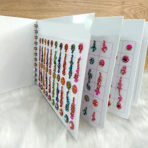 Puede incluir: Un libro con páginas de tatuajes temporales coloridos. Los tatuajes están dispuestos en filas y columnas en las páginas. Los tatuajes son de varias formas y tamaños, incluyendo flores, estrellas y patrones geométricos.