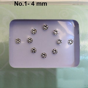 May include: A close-up of a small, clear plastic container with a light green background. The container holds nine small, clear rhinestones, each measuring 4 mm in diameter. The text "No. 1 - 4 mm" is printed on the container.