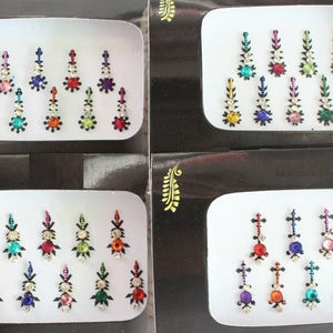 Puede incluir: Cuatro hojas de papel blanco con borde negro, cada una contiene un conjunto de 10 pegatinas de piedras preciosas de colores. Las pegatinas están dispuestas en filas y tienen forma de lágrima con un extremo puntiagudo.