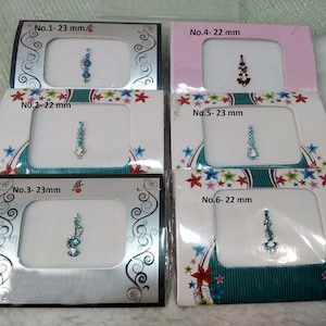 Puede incluir: Seis pequeñas tarjetas blancas con bordes de colores, cada una con un diseño de joyas diferente. Las tarjetas están etiquetadas con números y medidas en milímetros. Los diseños son para bindi, un adorno decorativo para la frente.