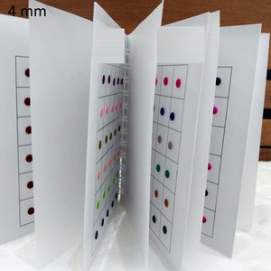 May include: A book with pages displaying a variety of small, round, colored stickers. The stickers are arranged in a grid pattern on each page. The book is labeled "4 mm" on the cover.