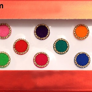 Könnte beinhalten: Eine Folie mit 12 bunten, runden, selbstklebenden Bindi-Stickern, jeder mit einem Durchmesser von 12 mm. Die Bindi-Sticker sind in zwei Reihen zu sechs angeordnet, mit einer Vielzahl von Farben, darunter Blau, Rosa, Lila, Grün, Orange, Rot, Gelb und Gold. Die Folie ist mit "d.no.1 - 12 mm" beschriftet.