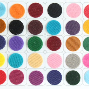 Può includere: Una cartella con 25 campioni di colore di tessuto, ognuno con un diametro di 11 mm. I campioni sono disposti in cinque file di cinque, con ogni fila che presenta uno schema di colore diverso. I colori includono rosso, arancione, giallo, verde, blu, viola, marrone, nero, bianco e rosa.