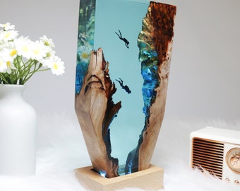 May include: A resin sculpture of a tree trunk with blue and green resin filling the space, depicting a scene of divers in the ocean. The sculpture is on a wooden base.