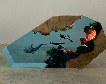 May include: A wooden and resin sculpture of an underwater scene with a whale shark, divers, and coral. The sculpture is lit from behind, creating a glowing effect.