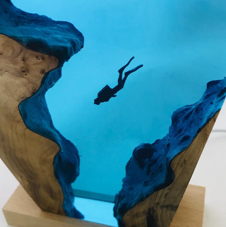 K&ouml;nnte beinhalten: Holzskulptur mit einer Taucher-Silhouette in einem blauen Harz-Ozean. Das Holz hat eine nat&uuml;rliche Maserung und ist mit blauem Harz akzentuiert, wodurch eine einzigartige Unterwasserszene entsteht. Auf einem Holzsockel montiert.
