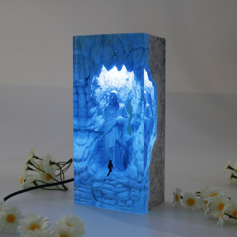 May include: A blue resin lamp with a 3D image of a person inside a cave. The lamp is lit from the inside, casting a blue glow.