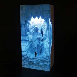 May include: A blue resin sculpture of a figure standing in a cave-like structure. The sculpture is illuminated from behind, creating a glowing effect.