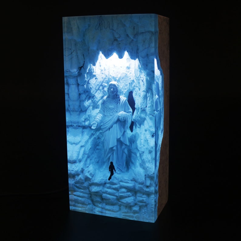 May include: A blue resin sculpture of a figure standing in a cave-like structure. The sculpture is illuminated from behind, creating a glowing effect.