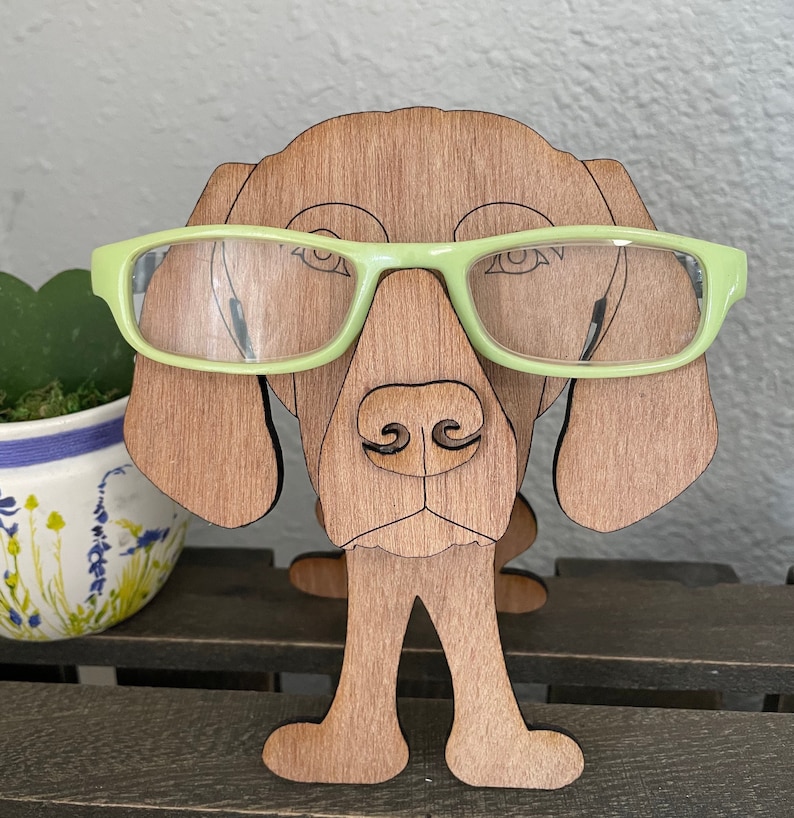 May include: A wooden dog figurine with a light green pair of glasses on its face. The dog has brown fur and is standing on four legs. The figurine is made of wood and has a natural wood finish.