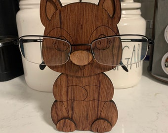 May include: A wooden cat figurine with a pair of glasses perched on its nose. The cat is brown with a wood grain pattern and has a cute, cartoonish face.