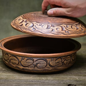 Peut inclure: Un pot en céramique brun avec un couvercle, tous deux décorés de motifs floraux noirs complexes. Le couvercle est légèrement entrouvert, révélant l'intérieur vide du pot.