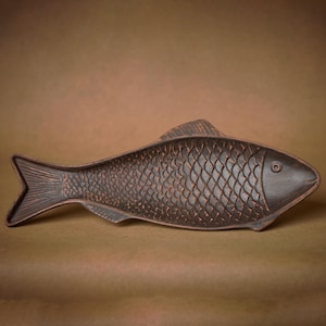 Può includere: Un piatto da portata in ceramica a forma di pesce di colore marrone scuro con una superficie testurizzata che ricorda le squame di pesce.