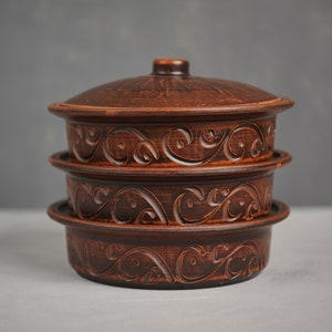 Op de afbeelding: Een set van drie bruine keramische kommen met ingewikkelde bloemmotieven. De kommen zijn op elkaar gestapeld, met de grootste kom onderaan en de kleinste kom bovenaan. De kommen hebben een rustieke, handgemaakte uitstraling.