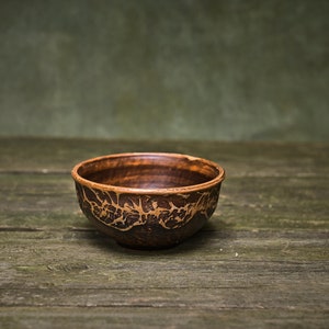 May include: A small, brown ceramic bowl with a decorative pattern. The bowl is sitting on a rustic wooden surface.