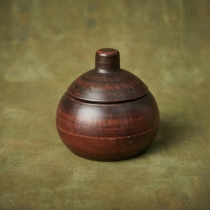 May include: A dark brown ceramic jar with a lid. The jar has a rounded shape and a smooth, matte finish.
