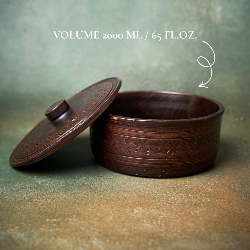 May include: A dark brown circular clay container with a matching lid, featuring an embossed vine pattern around the exterior and lid. The text VOLUME 2000 ML / 65 FL.OZ. is printed above the container, indicating a capacity of 65 fluid ounces.