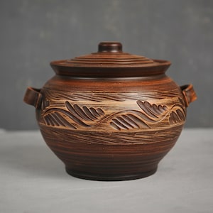 May include: A brown ceramic pot with a lid and two handles. The pot has a decorative design of leaves carved into the surface.