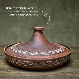 May include: A brown ceramic tagine pot with a lid. The pot is 6.3 inches tall with the lid, 11.4 inches in diameter, and 2.1 inches high. The lid and base feature decorative carved patterns. The text on the image reads: HEIGHT WITH LID: 6.3 IN, DISH DIAMETER: 11.4 IN, DISH HEIGHT: 2.1 IN.