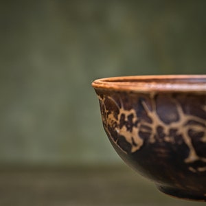 May include: A brown ceramic bowl with a decorative pattern of brown and white lines. The bowl is slightly tilted and the inside is visible.