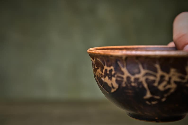 May include: A brown ceramic bowl with a decorative pattern of brown and white lines. The bowl is slightly tilted and the inside is visible.