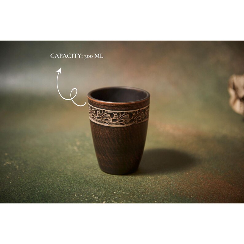 May include: A dark brown ceramic cup with a decorative band near the top. The band features a white and brown floral design. The cup has a capacity of 300 ml.